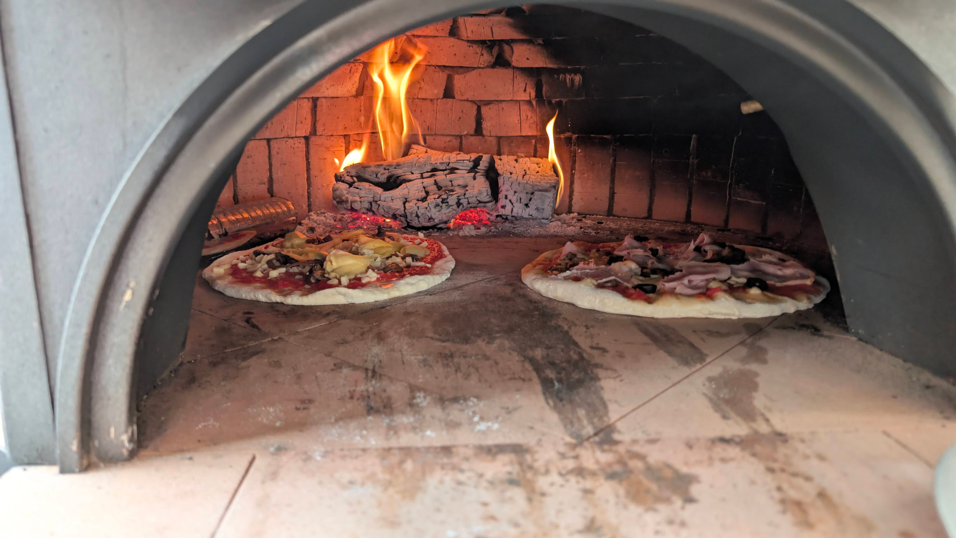 Twee pizza's bakken op de steen van de houtoven naast het vuur