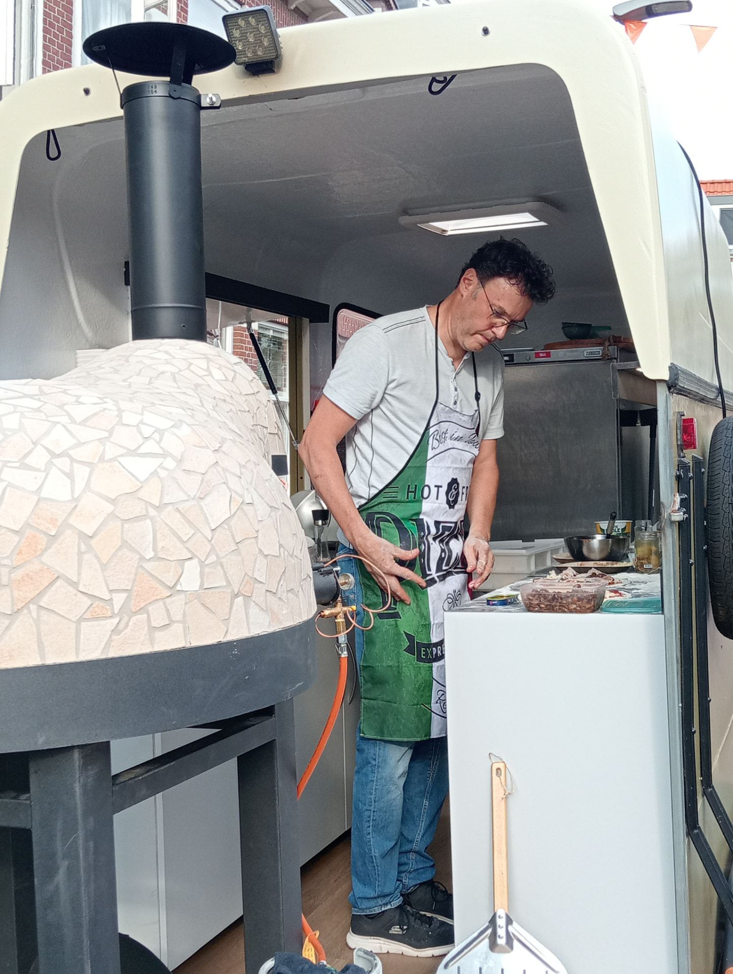 Frans bereidt de pizza's naast de houtoven in de pizzatrailer