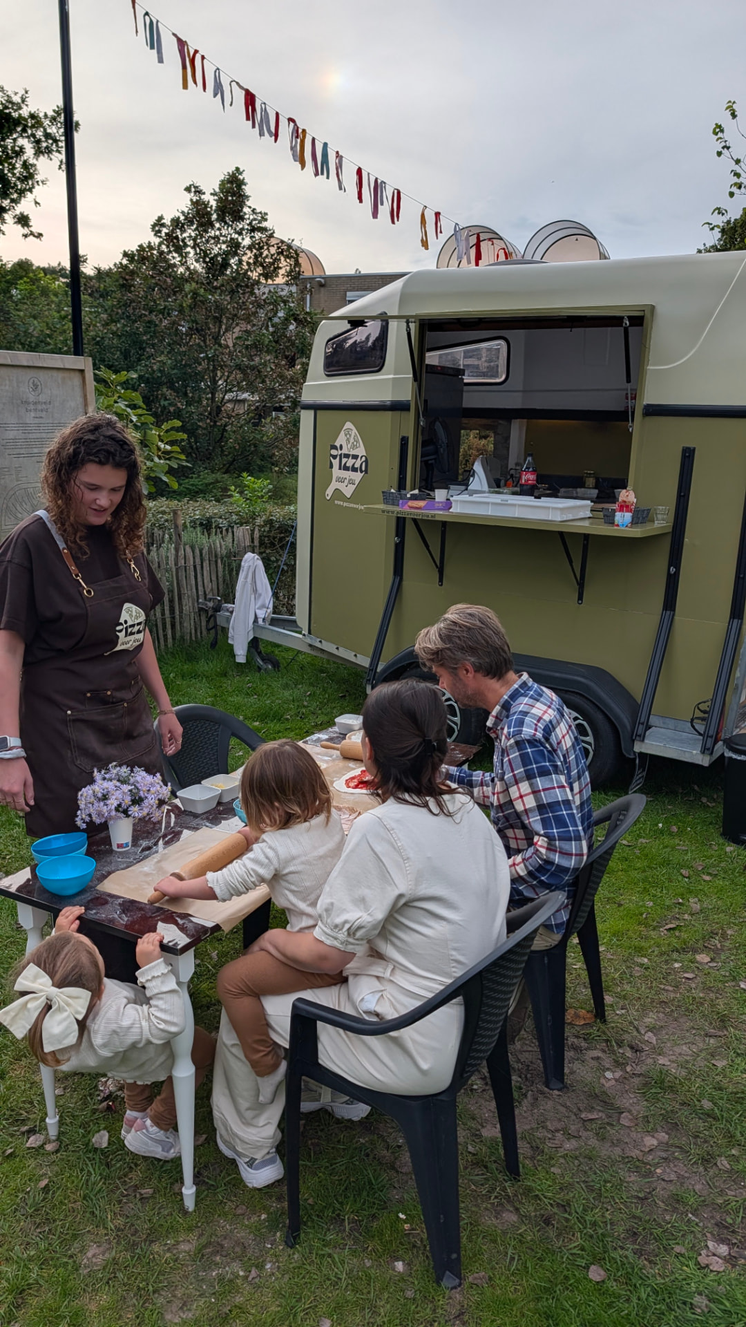 Frans van Pizza voor jou bakkt pizza's met een gezin naast de pizzatrailer in Bentveld