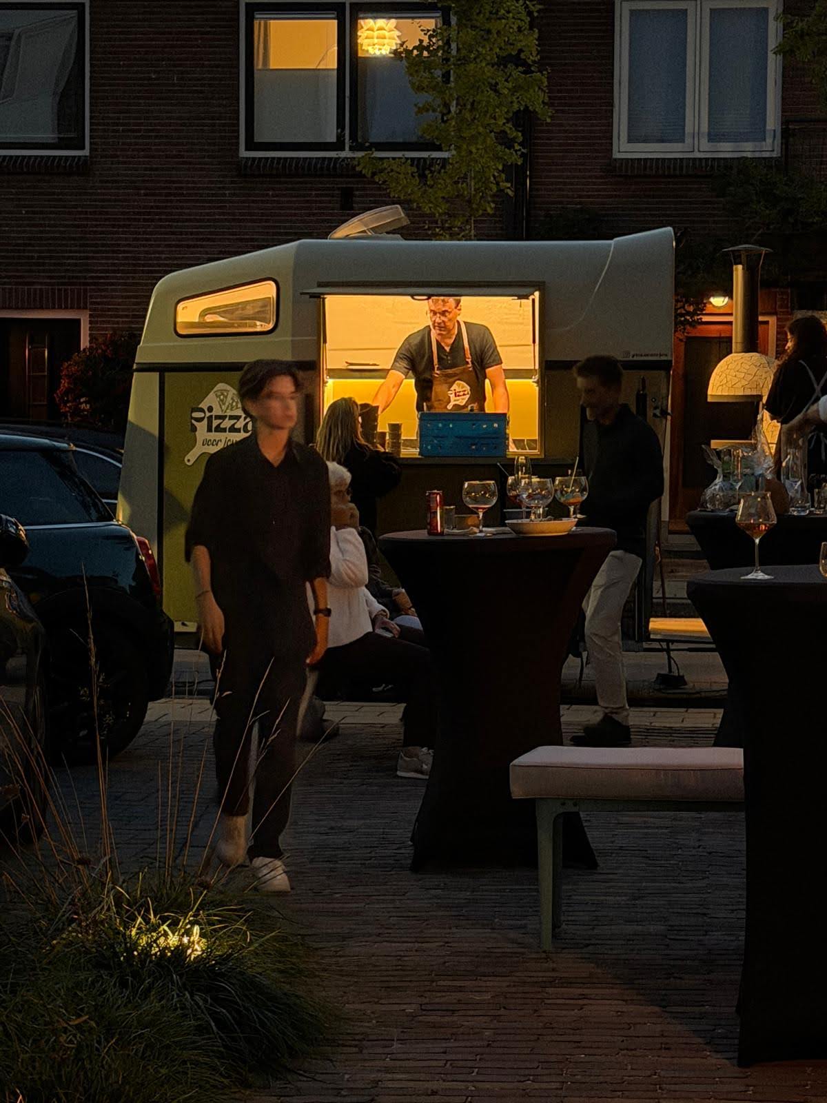 De verlichte pizzatrailer van Pizza voor jou 's avonds in Gouda, met gasten aan de statafels